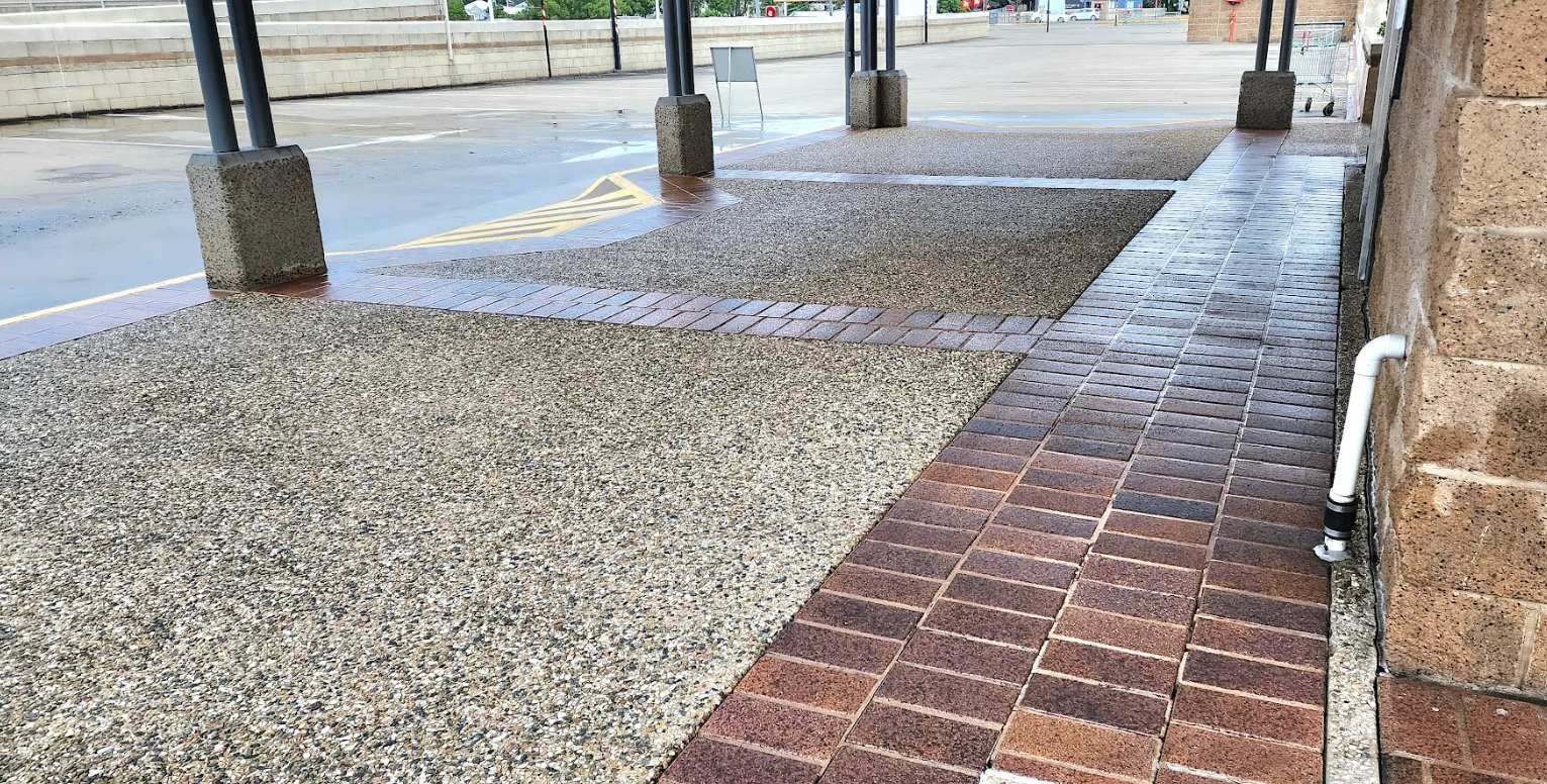 A paved walkway with a brick path running alongside areas of decorative gravel beneath a covered outdoor structure.