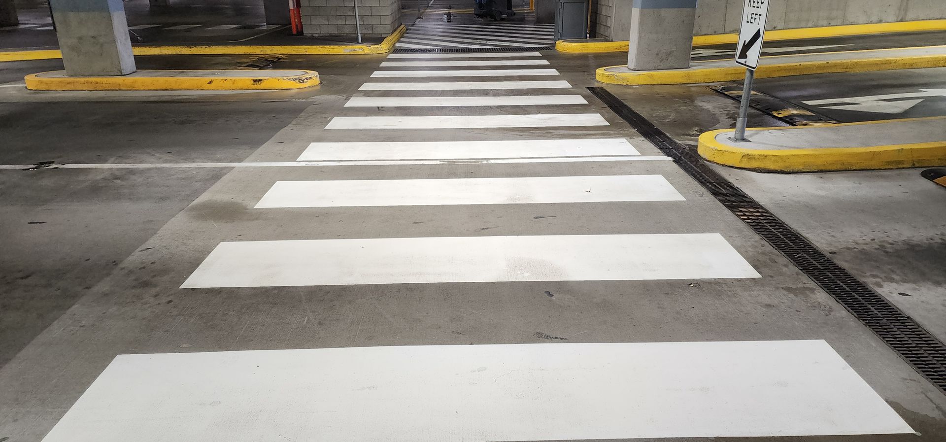 A white painted pedestrian crosswalk in a parking garage with yellow-bordered concrete pillars.