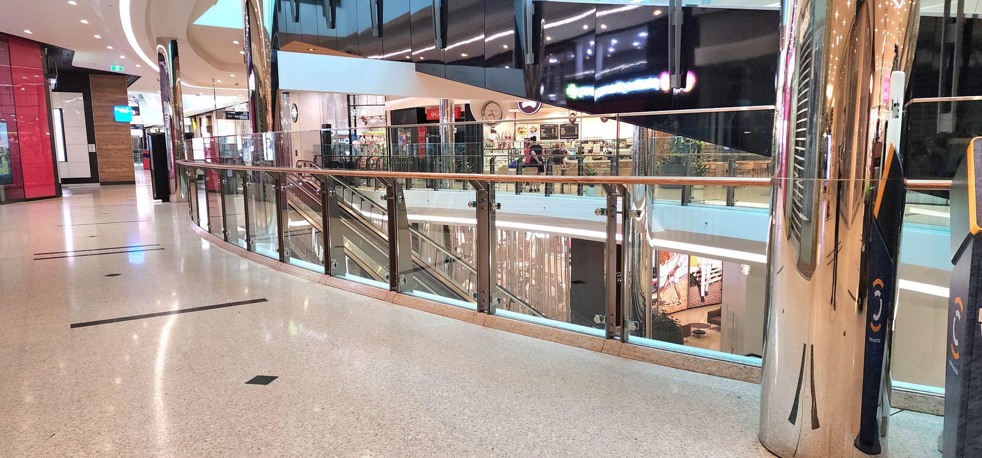 A modern, multi-level indoor shopping mall with polished light-colored floors, glass railings, and reflective columns.