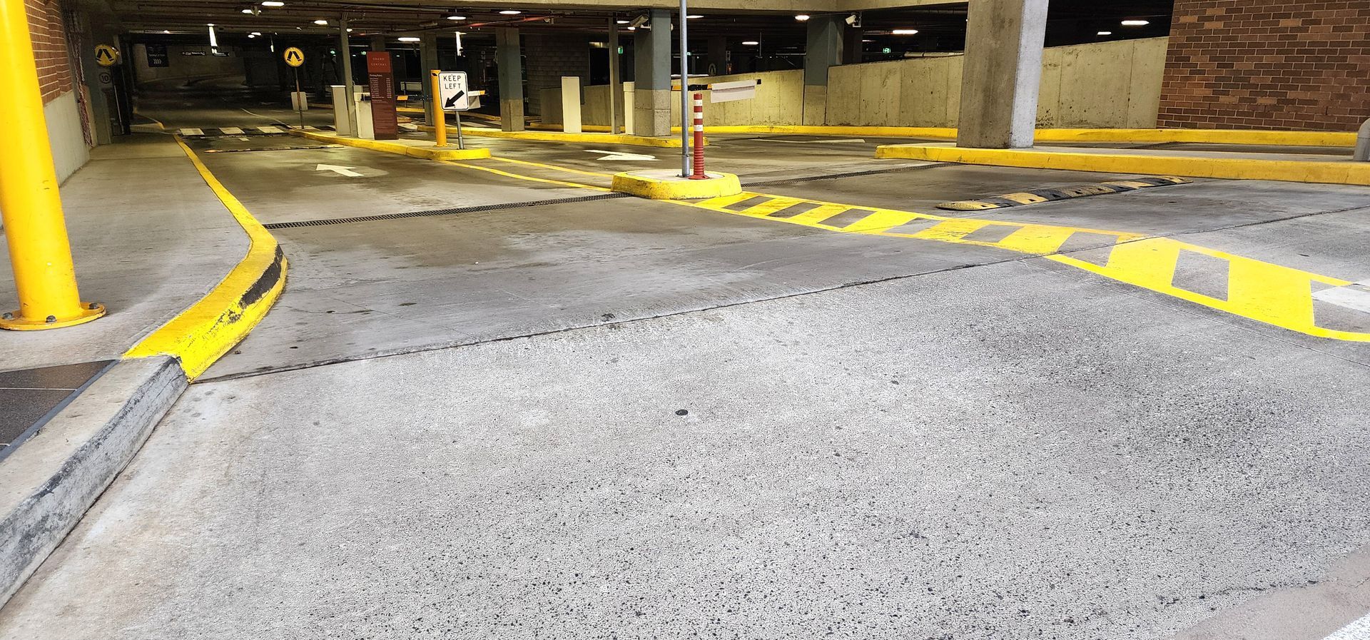 The entrance to an indoor parking garage with concrete pavement and bright yellow painted safety markings.