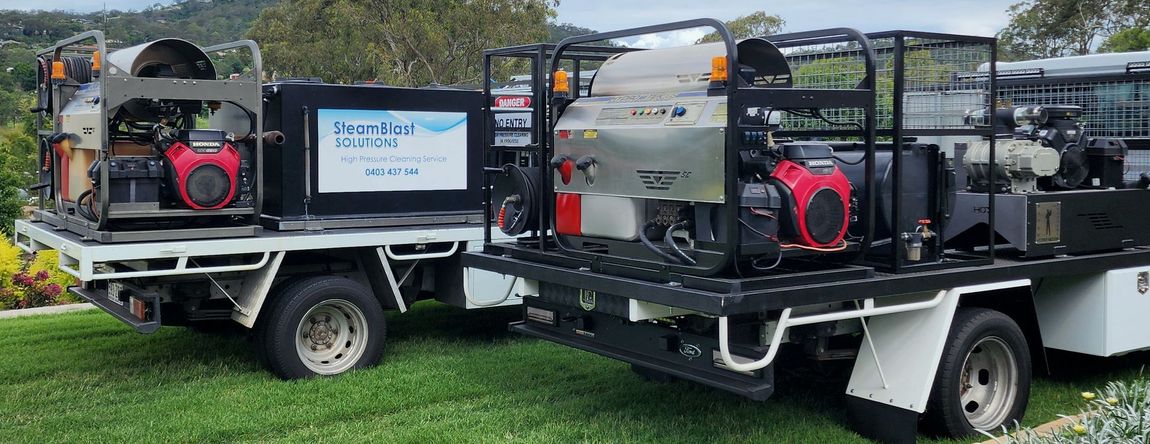 Two pickup trucks with cleaning equipment on the beds parked on green grass.