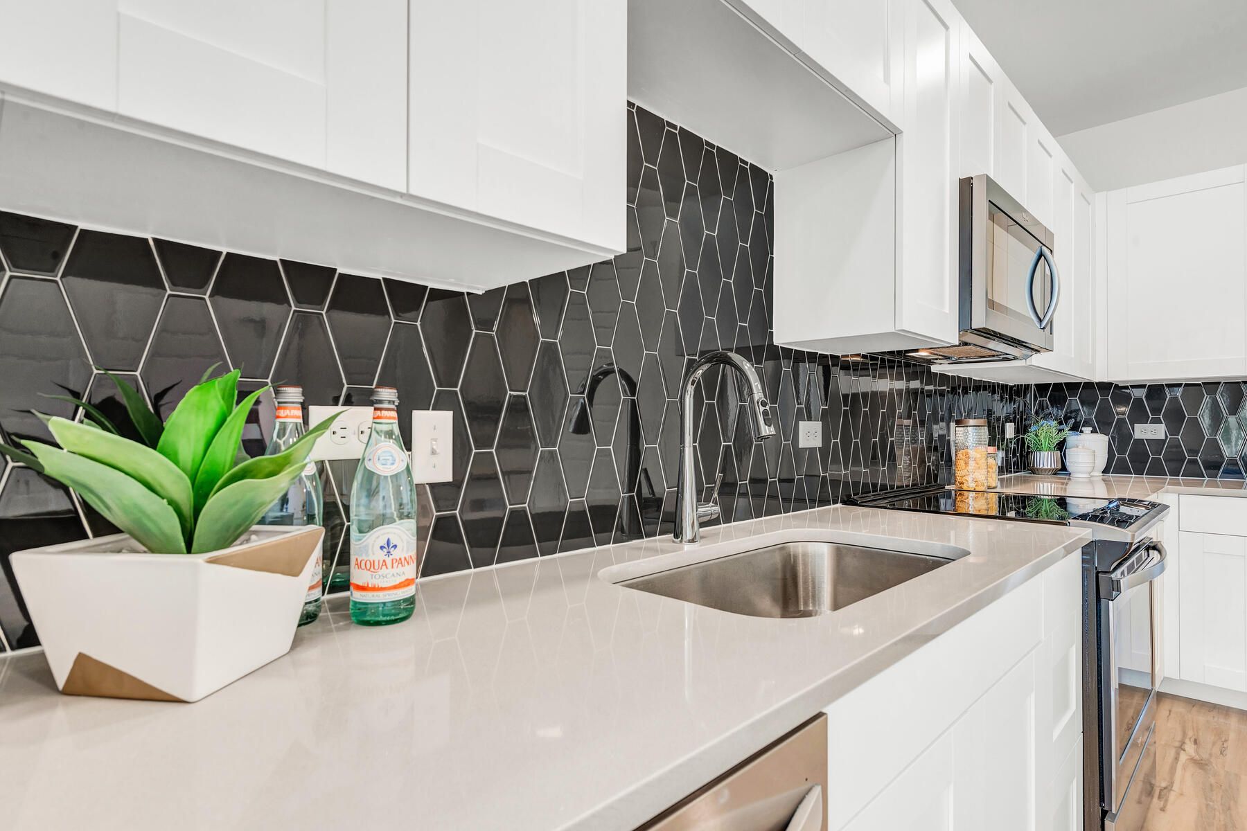 Modern kitchen with white cabinets, dark tile backsplash, and stainless steel sink.