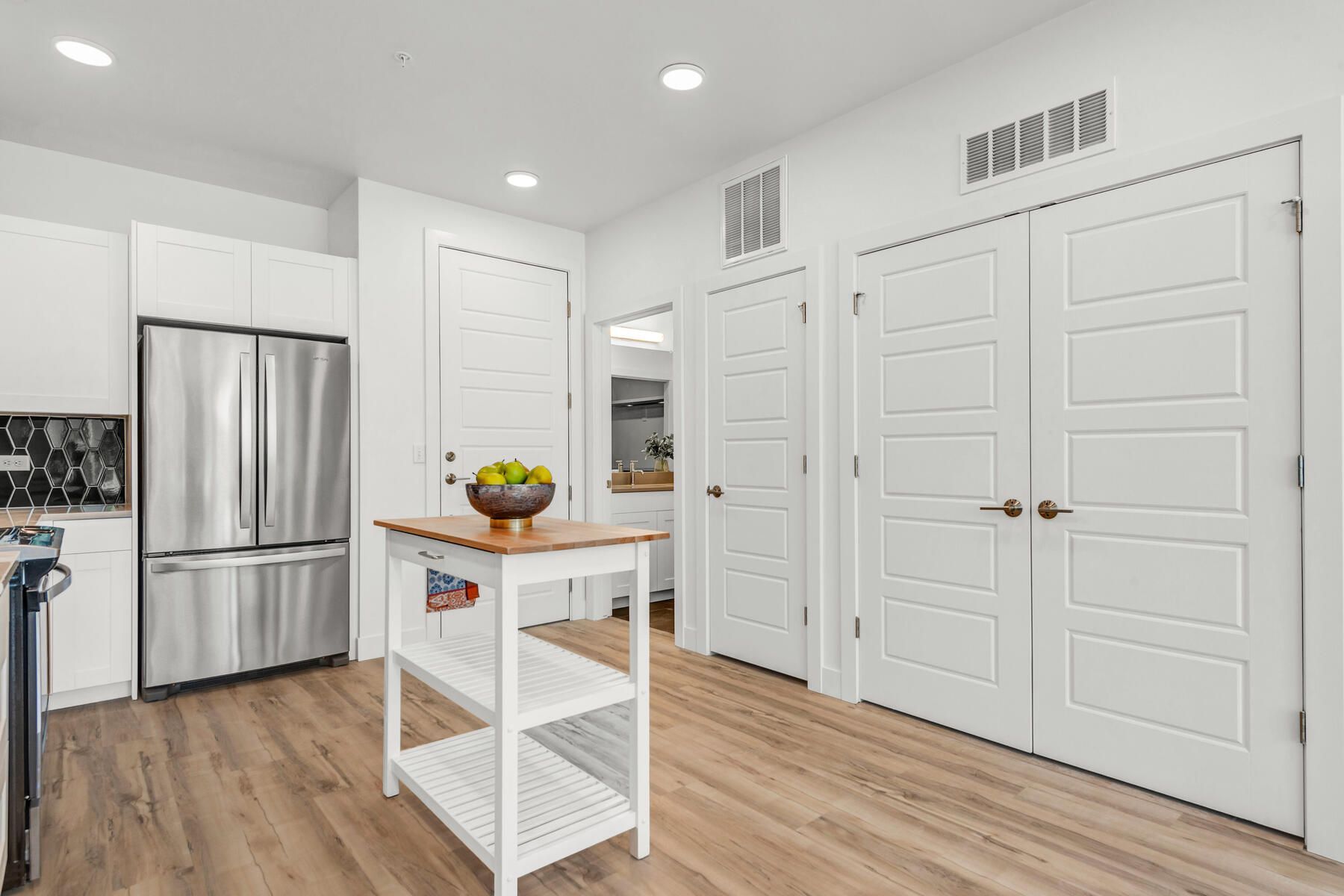 Kitchen with white cabinets, stainless steel refrigerator, and wood-look flooring. White island with fruit.