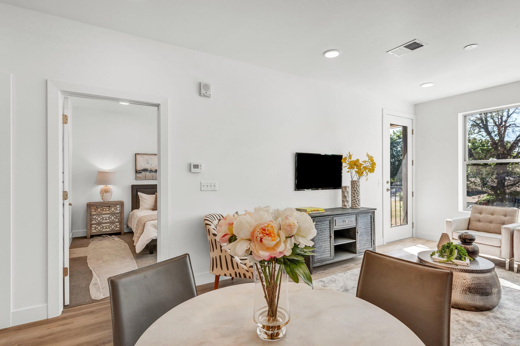 Living room with dining table, TV, and open doorway to a bedroom; bright, airy space.