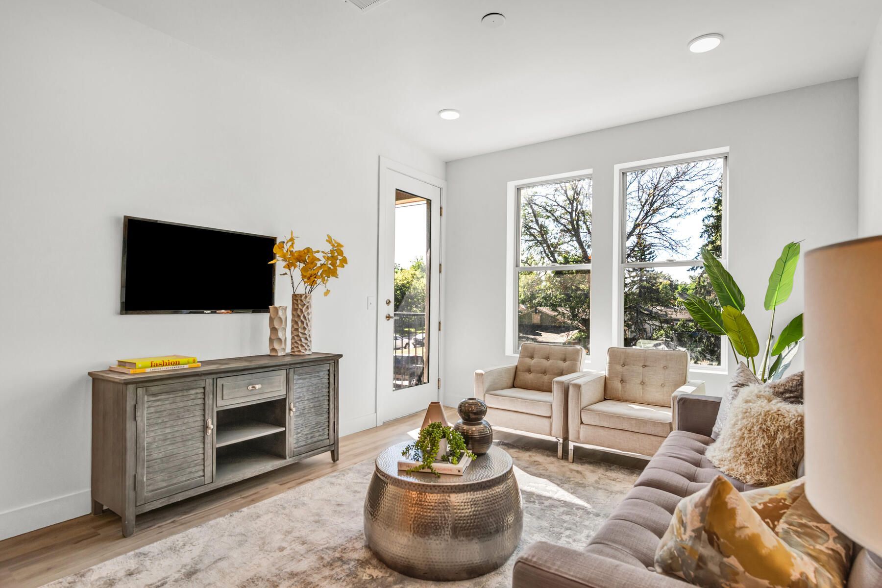 Living room with gray sofa, armchairs, coffee table, TV, and large windows with a view.