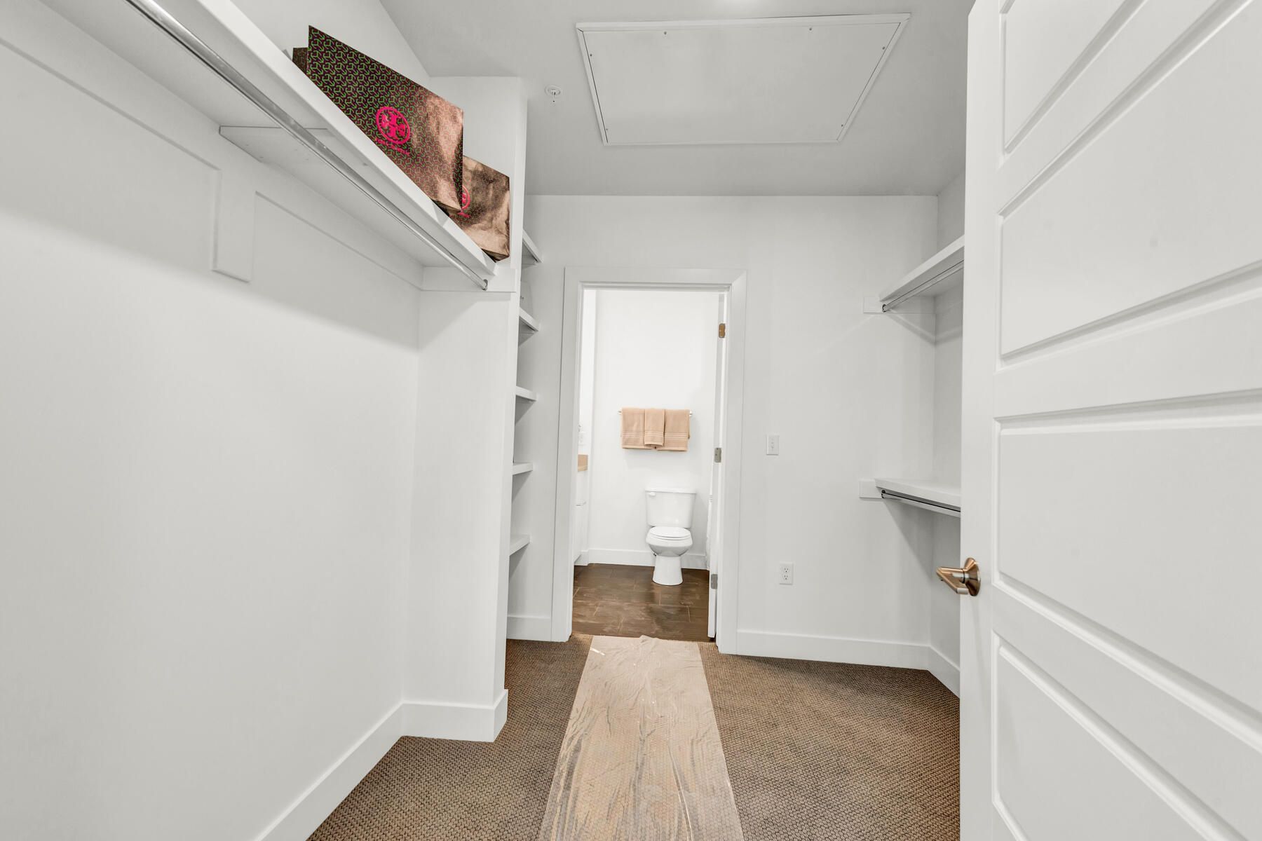 Walk-in closet with white shelves and walls; a doorway leads to a toilet room with towels.