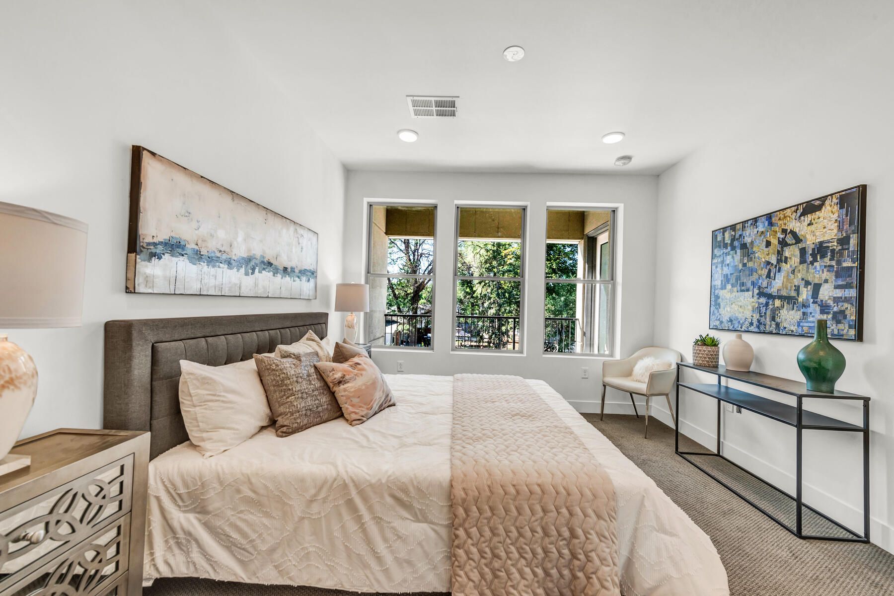 Bedroom with a bed, artwork, and large windows overlooking trees; white walls and neutral decor.