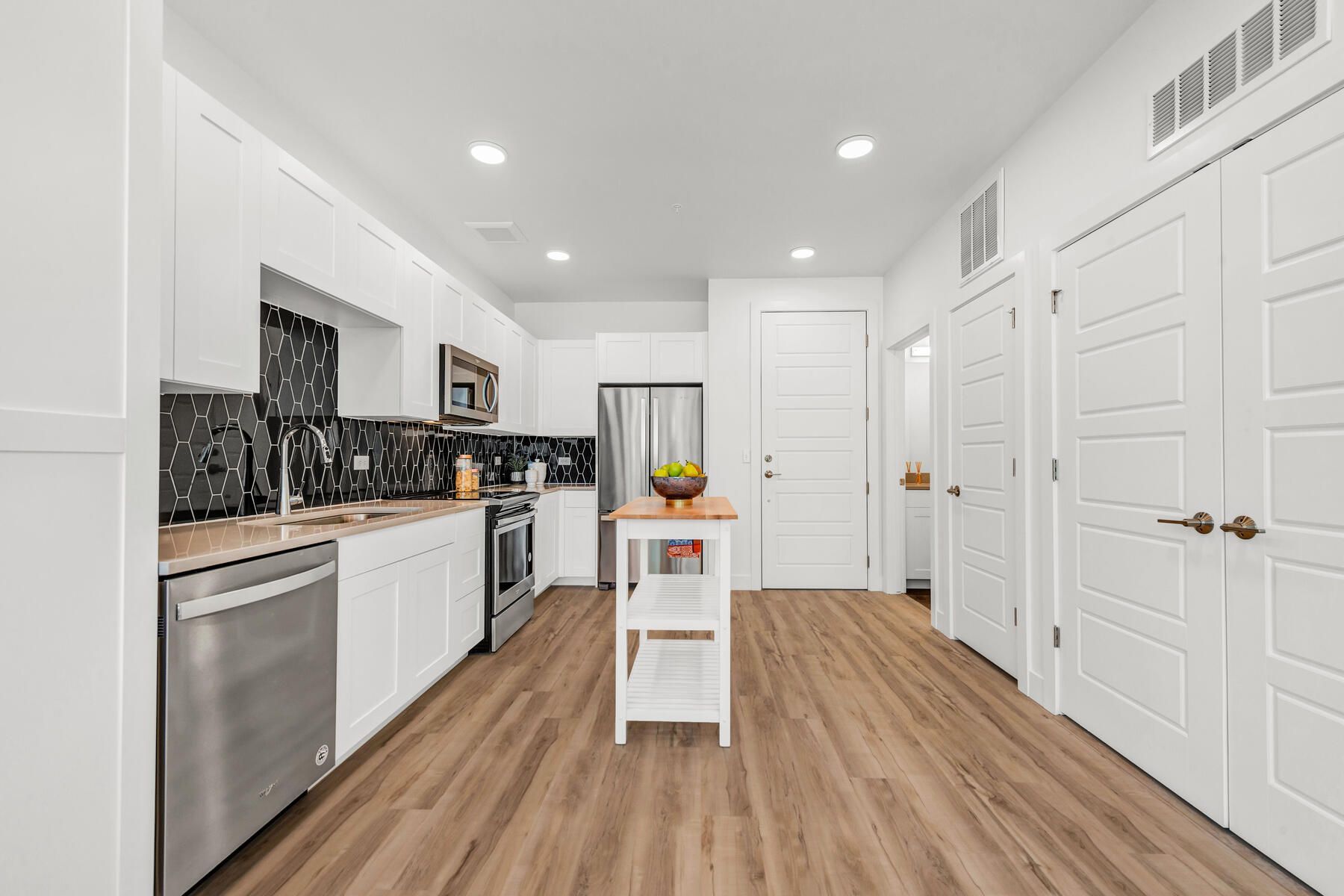 Modern white kitchen with stainless steel appliances, wood floor, and small island.