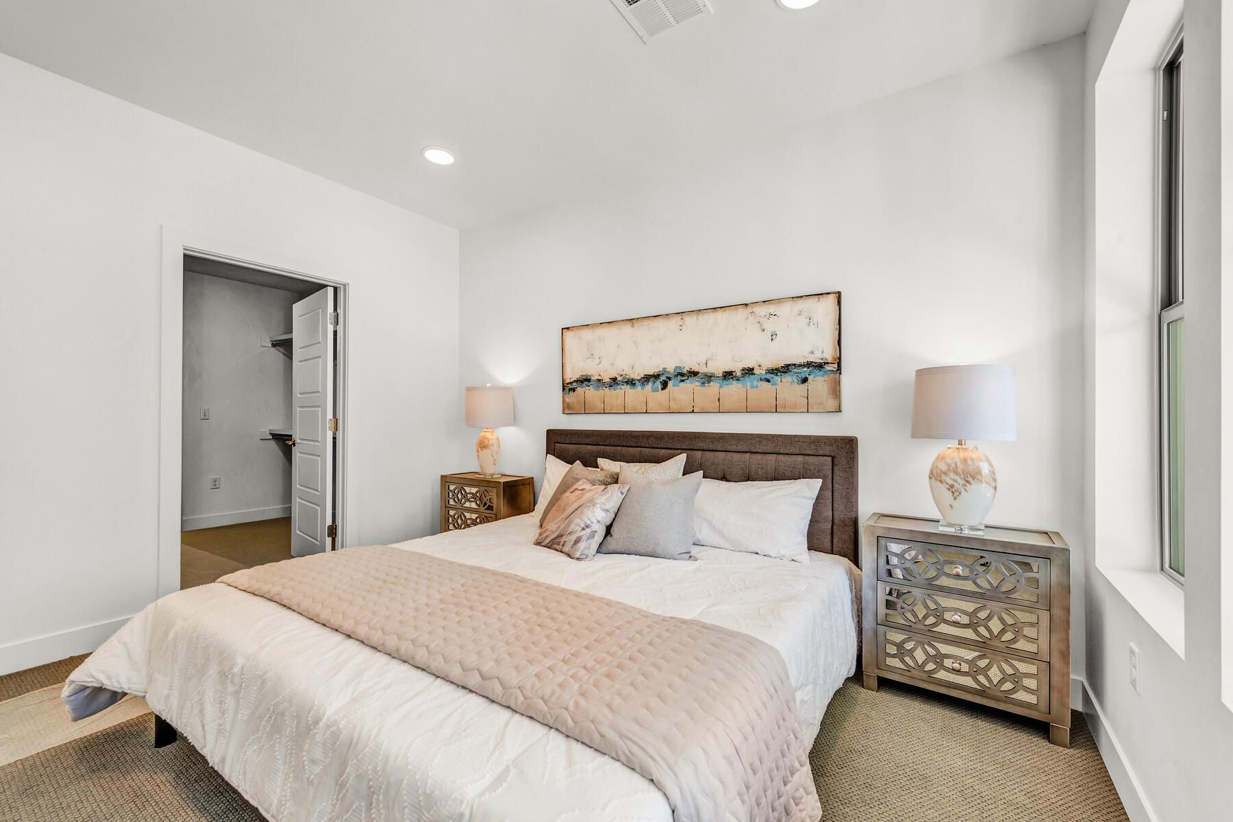Bedroom with a bed, nightstands, artwork, and a walk-in closet. The room is painted white.