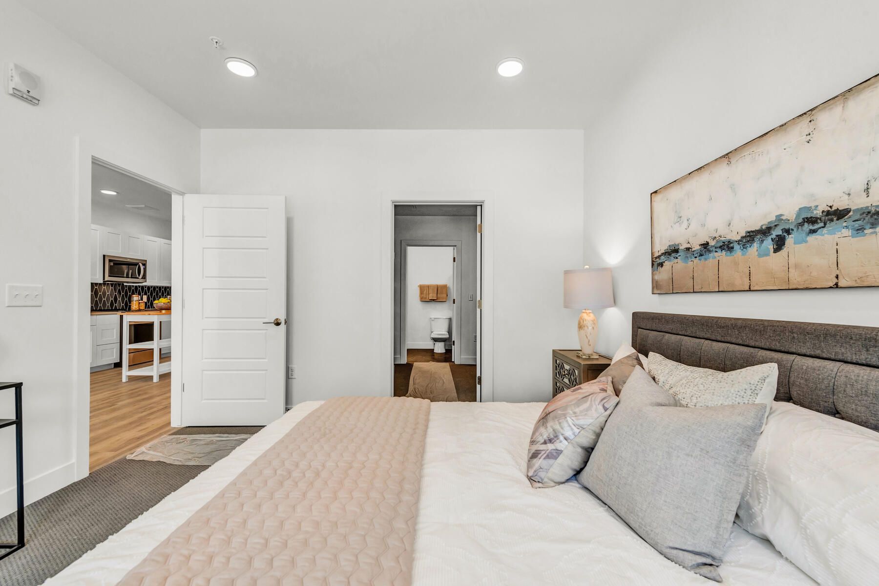 Bedroom with bed, pillows, artwork, doorway to kitchen and bathroom.