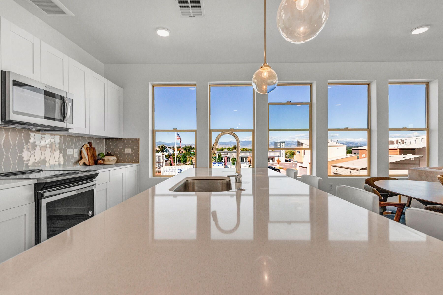 Bright kitchen with large island, stainless steel appliances, and city view through windows.