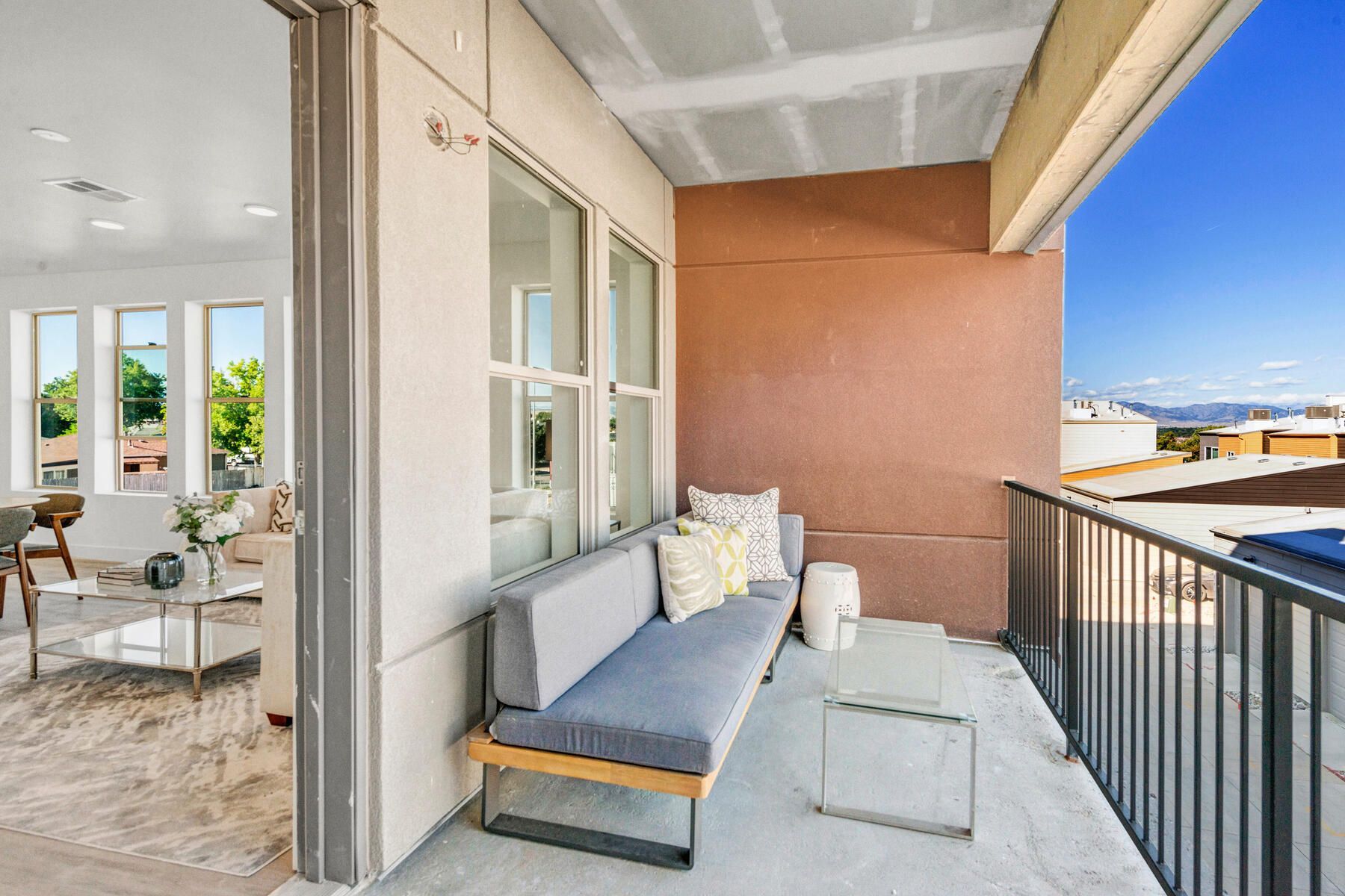 Balcony with gray sofa, white side table, and metal railing overlooking a cityscape.