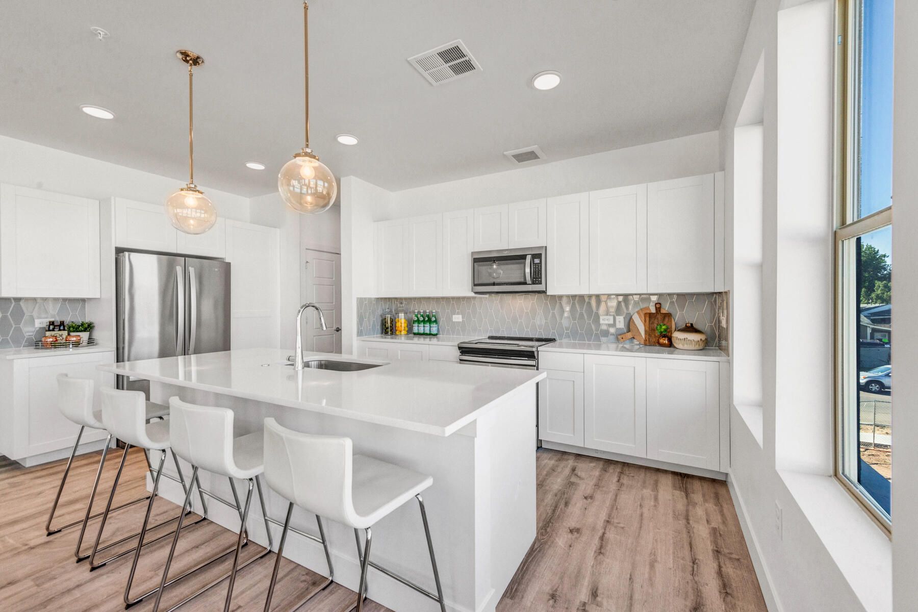 Modern white kitchen with island, stainless steel appliances, and wood flooring.