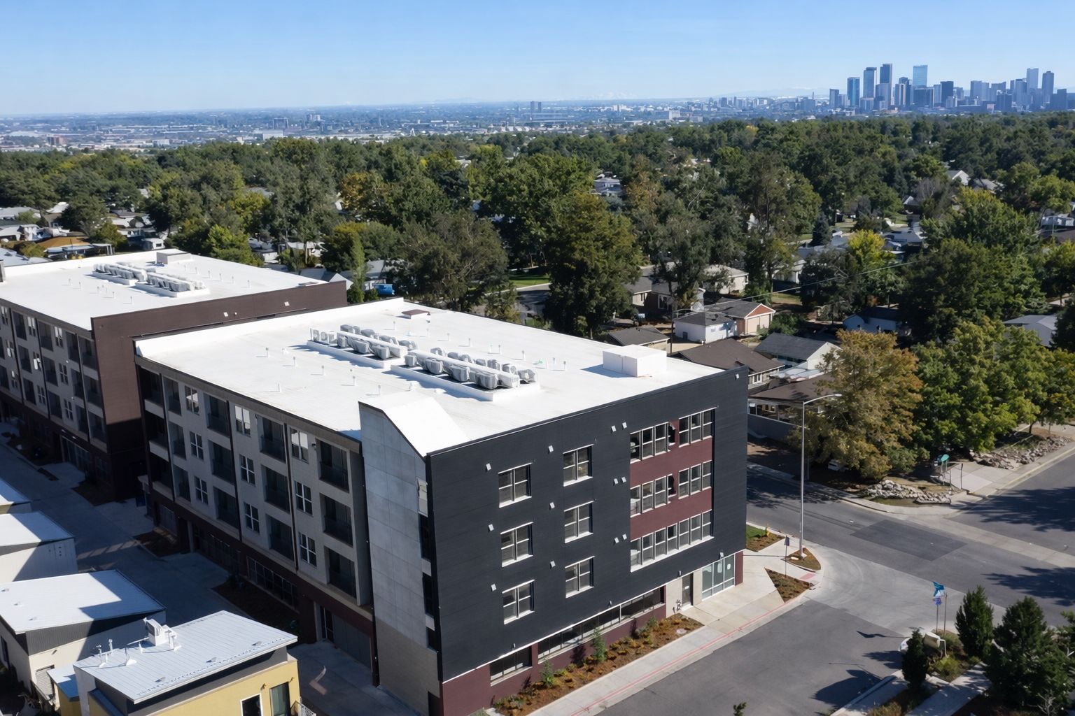 Modern apartment building overlooking a city skyline and trees on a sunny day.