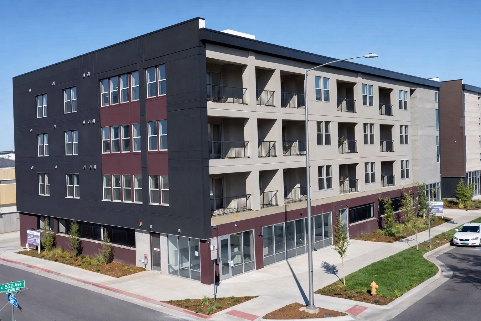 Modern apartment building with black, gray, and red exterior; street level retail; balconies.