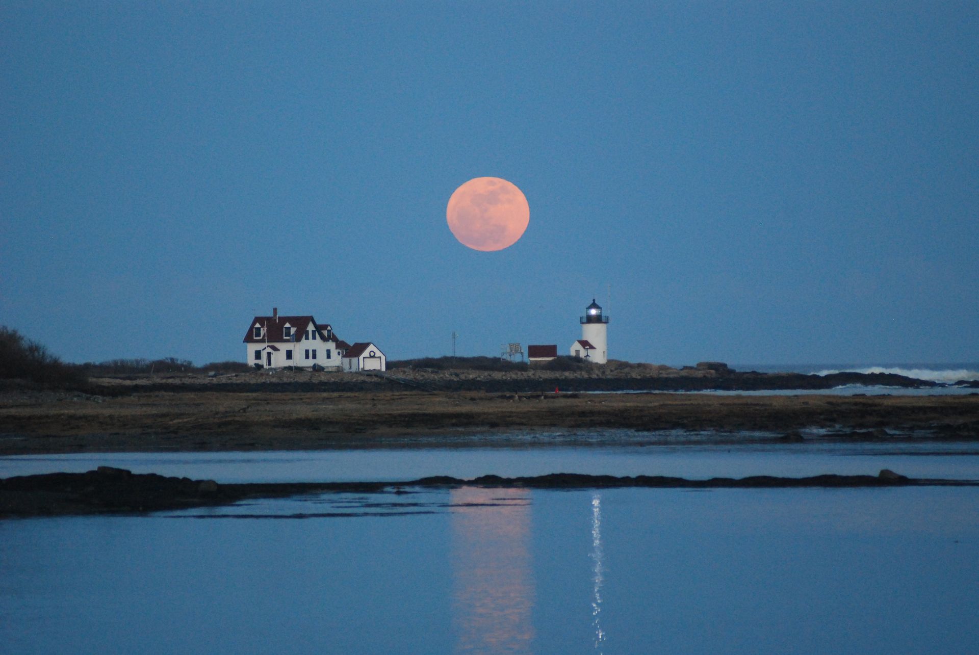 A full moon is rising over a lighthouse and a house