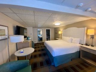 A hotel room with a king size bed , chair , table and television.