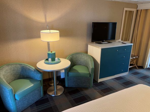 A hotel room with two chairs , a table , a lamp and a television.