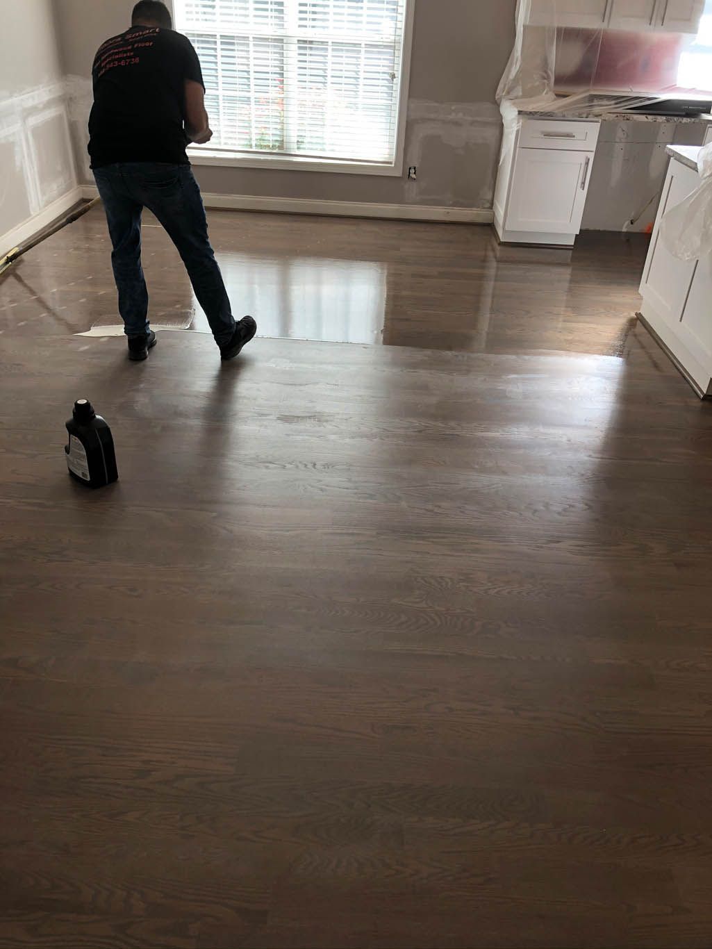 A man is standing on a wooden floor next to a cat.