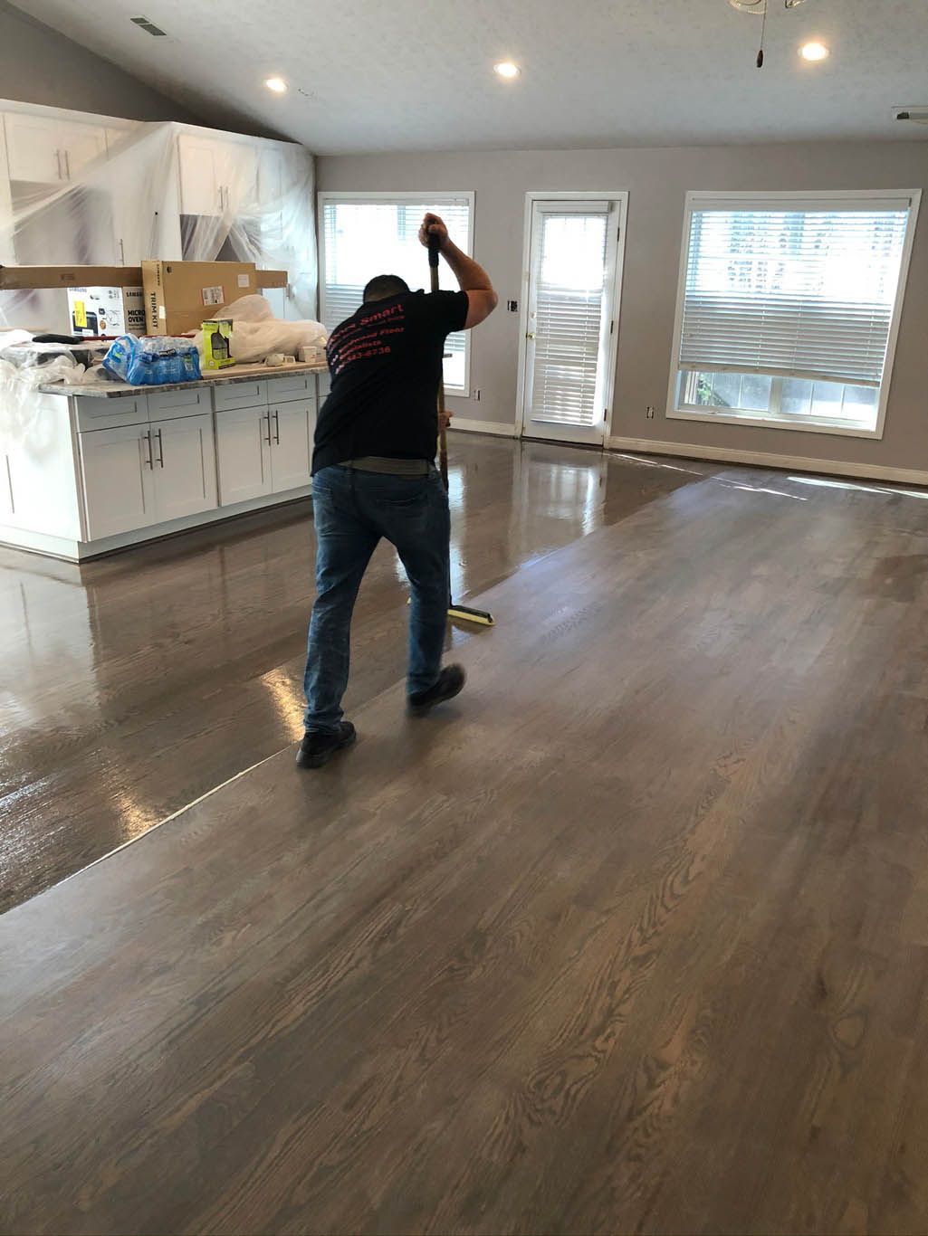 A man is painting a wooden floor in a living room.