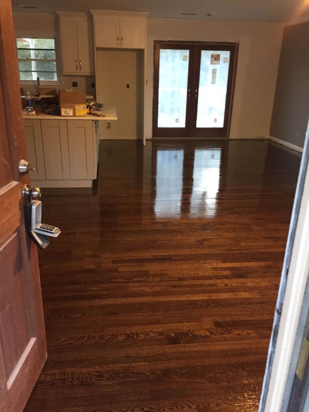 A living room with hardwood floors and a kitchen in the background.
