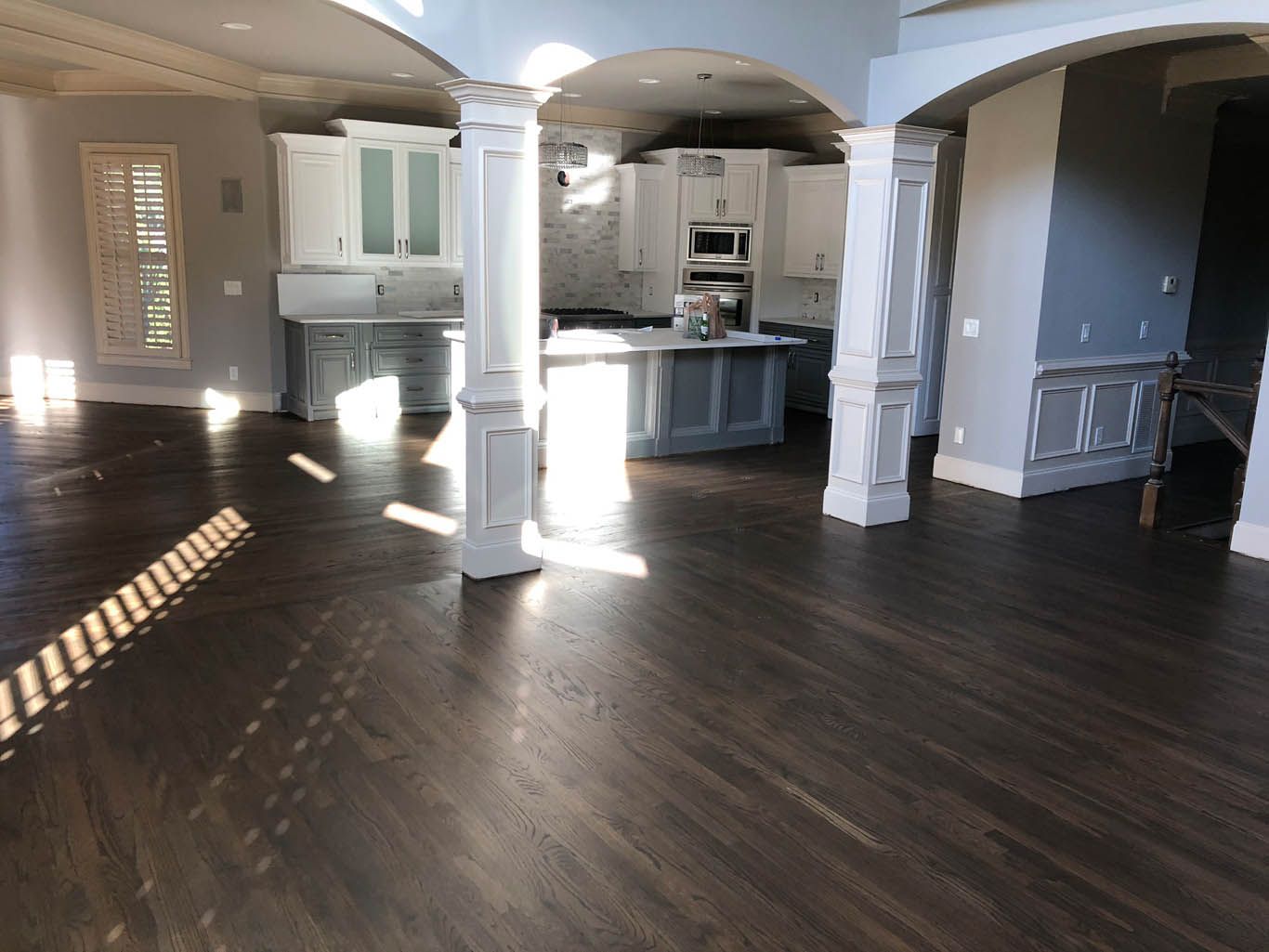 A large empty room with hardwood floors and a kitchen in the background.
