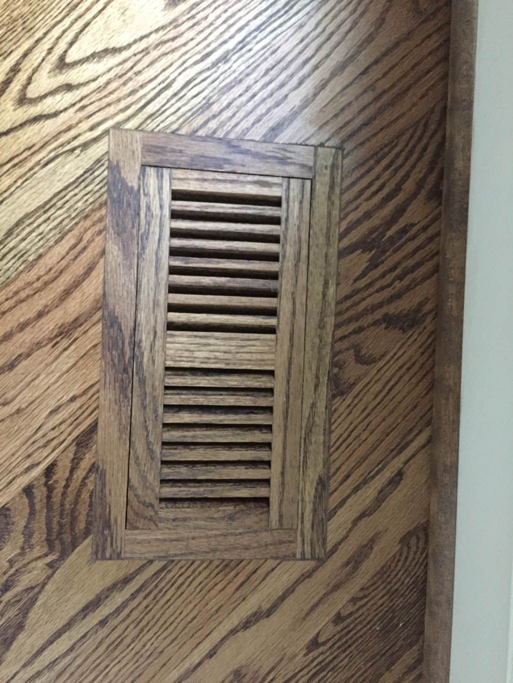 A wooden air vent on a wooden floor in a room.