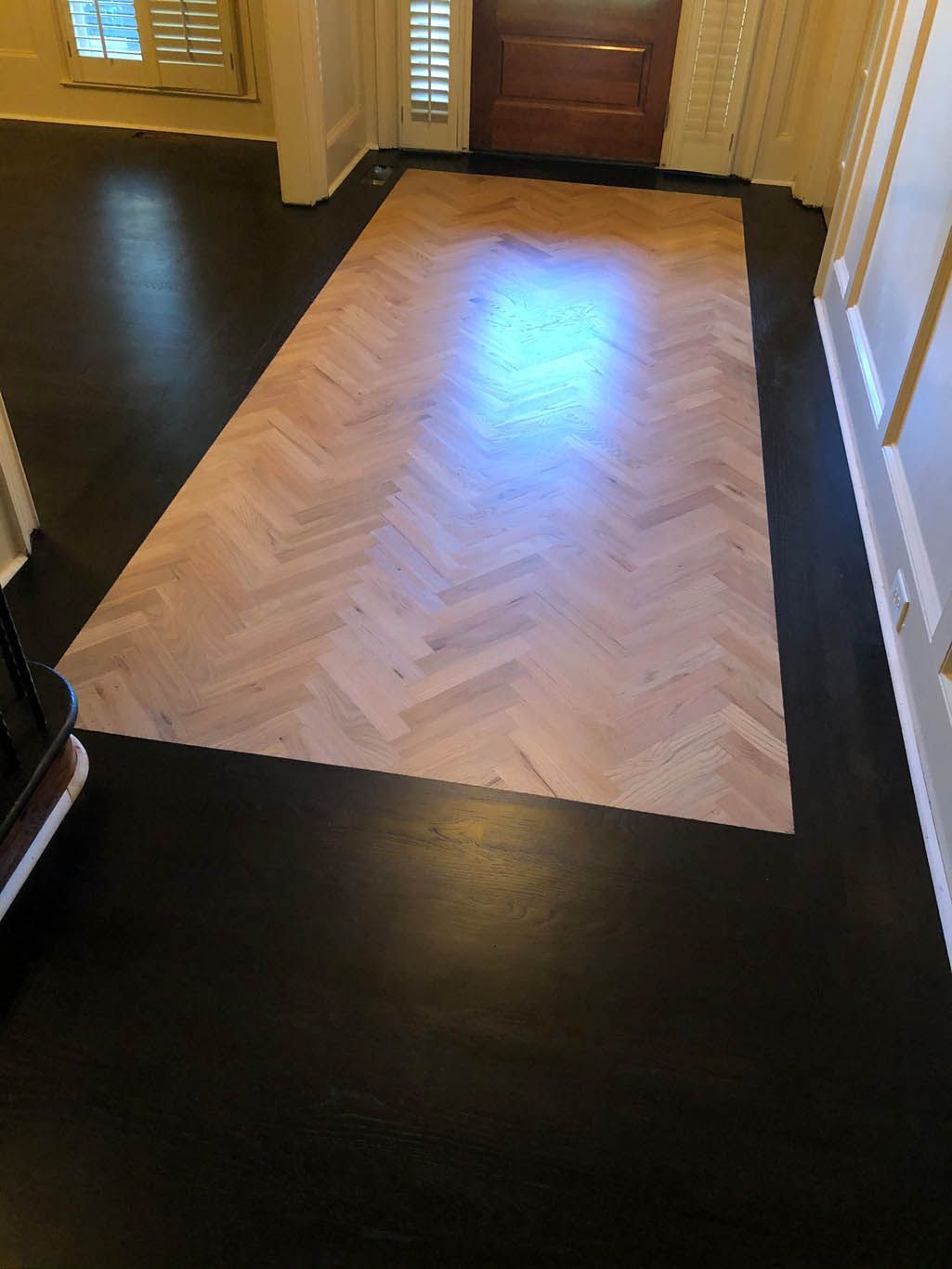 A wooden floor with a herringbone pattern in a hallway.