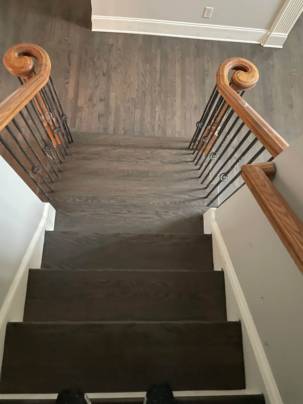 A wooden staircase with a wooden railing and a person standing on the bottom of the stairs.