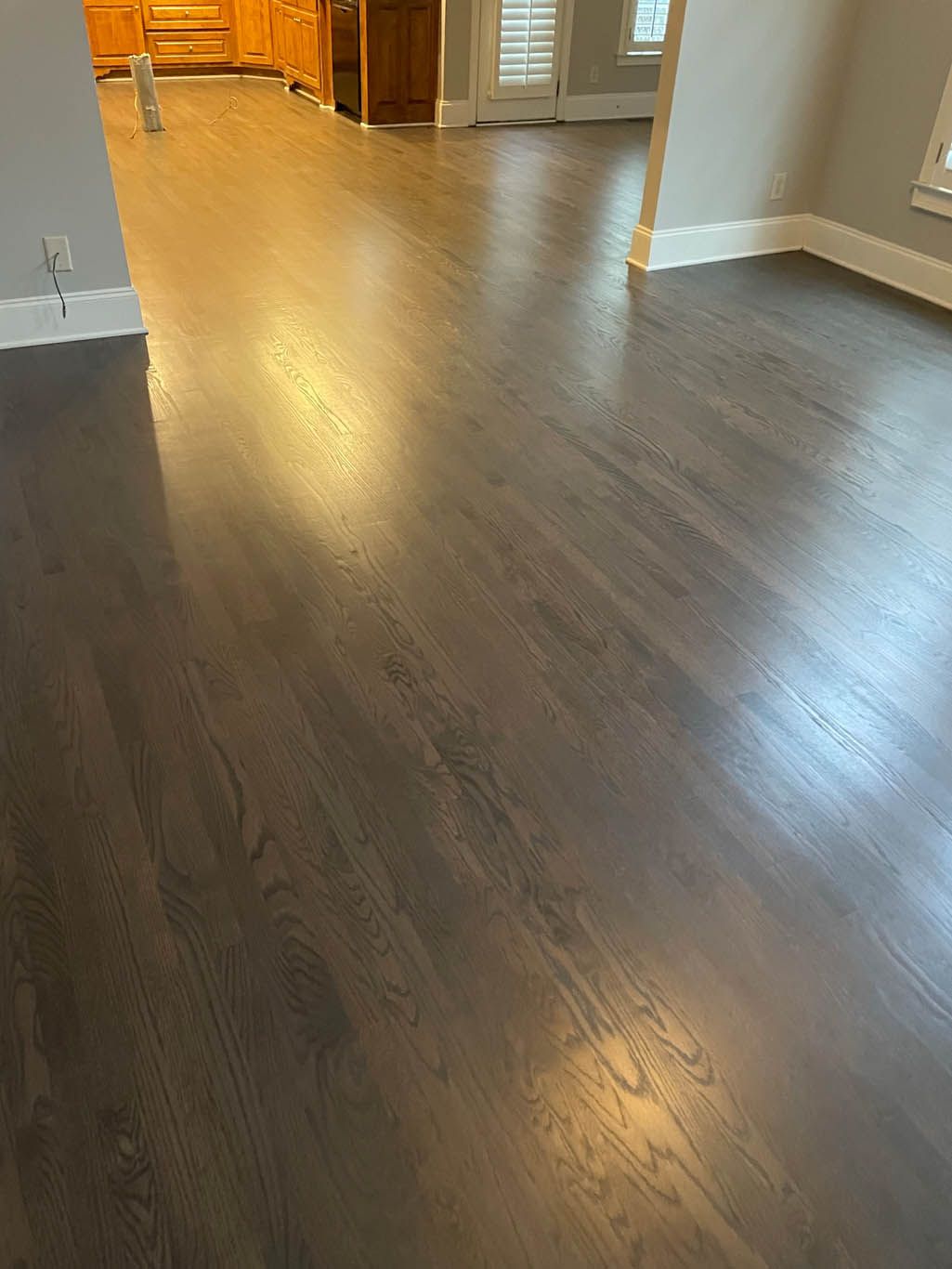 A living room with hardwood floors and a kitchen in the background.
