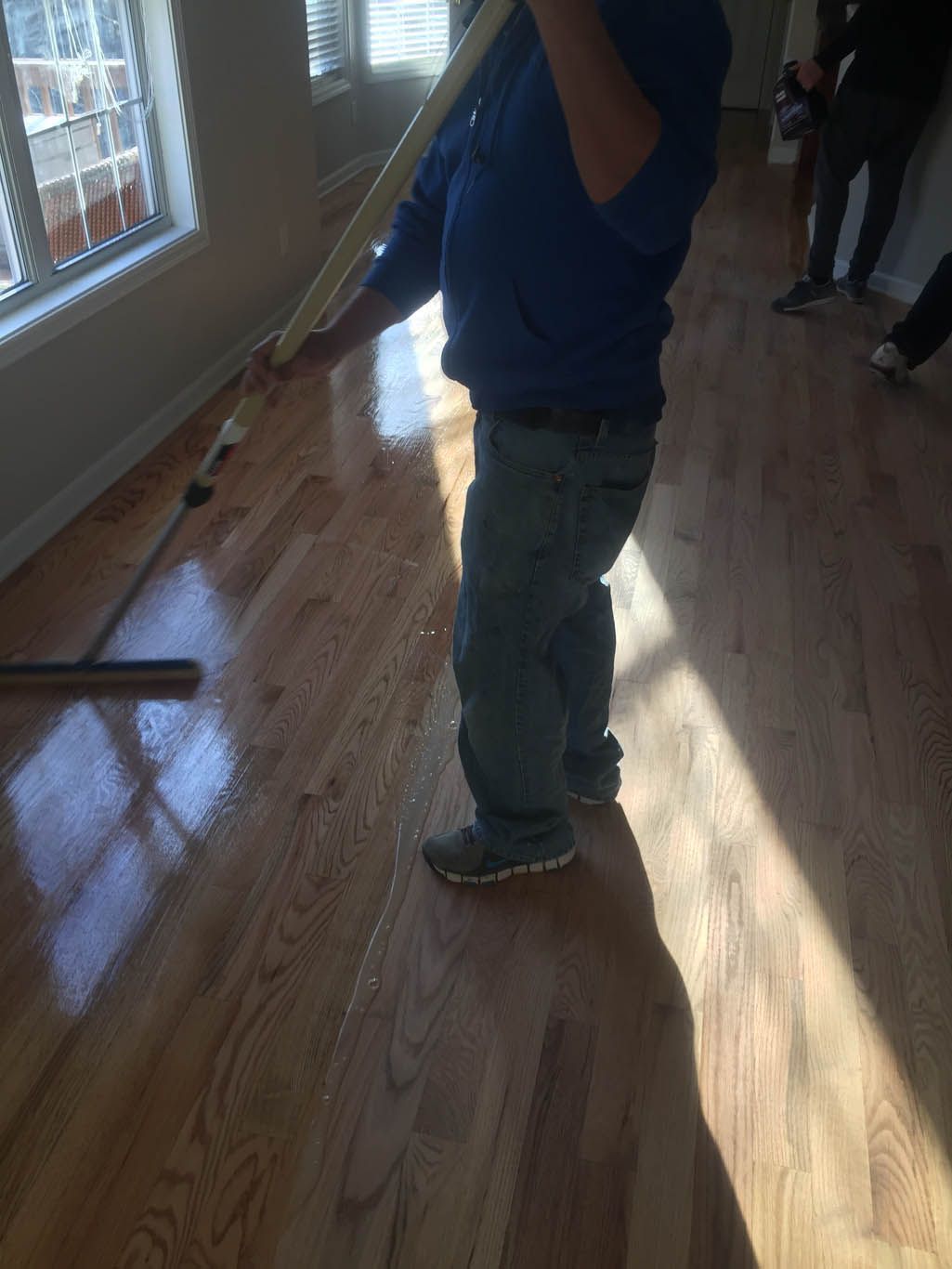 A man in a blue shirt is standing on a wooden floor holding a broom.