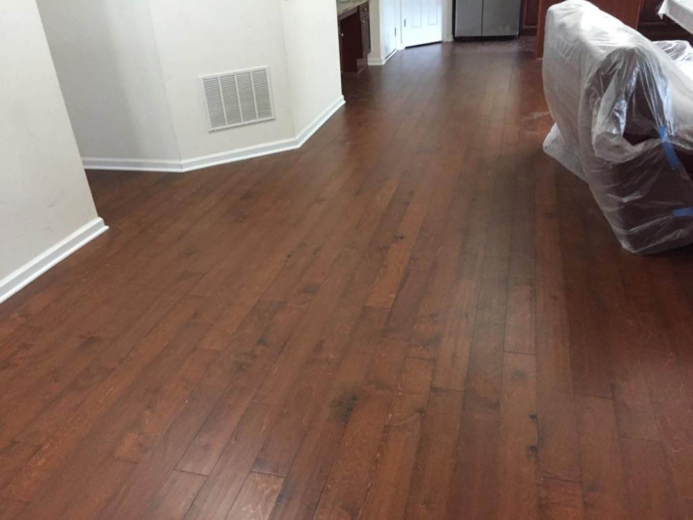 A living room with hardwood floors and a couch wrapped in plastic.