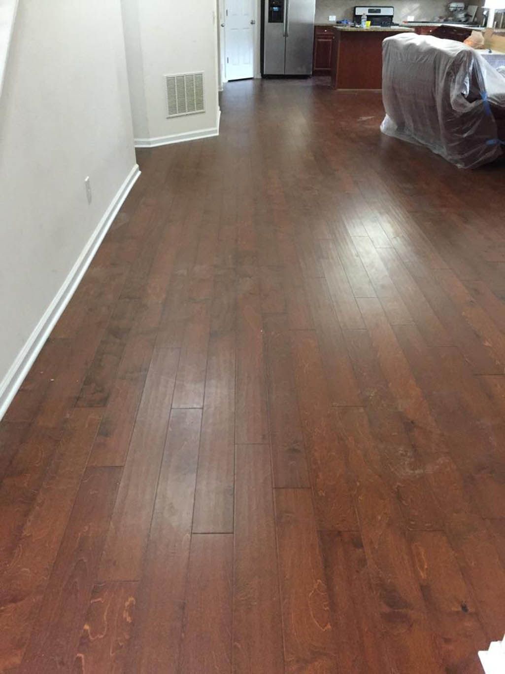 A living room with hardwood floors and a couch covered in plastic.