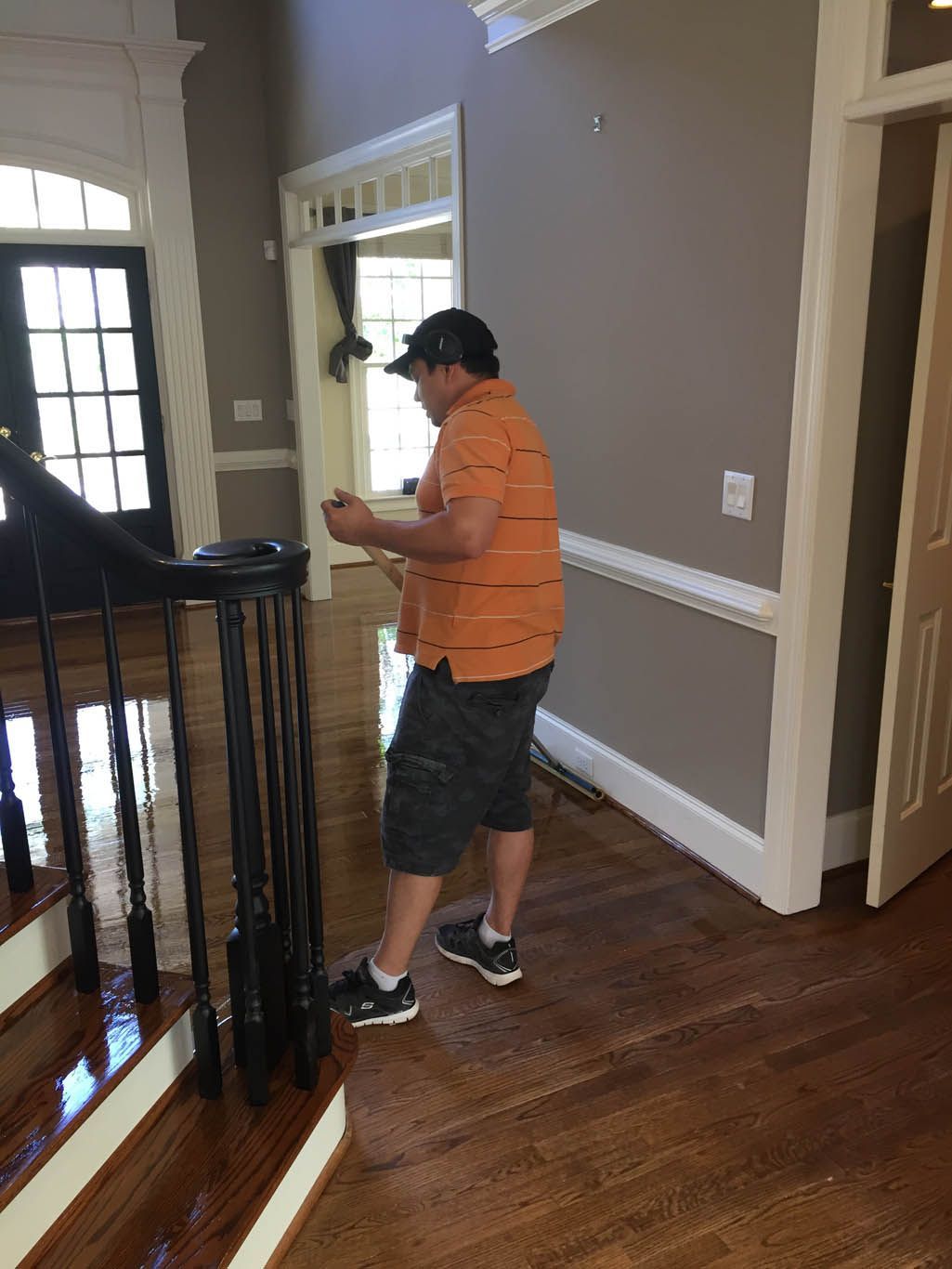 A man is standing on a wooden floor in a room next to stairs.
