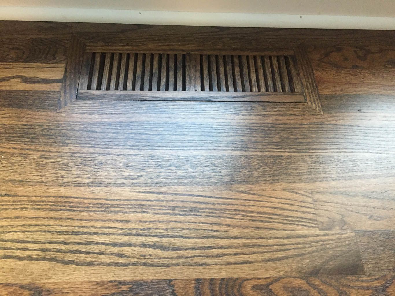A close up of a wooden floor with a vent on it.