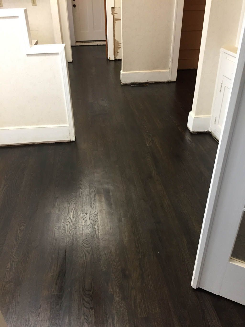 A hallway with a dark wood floor and white walls