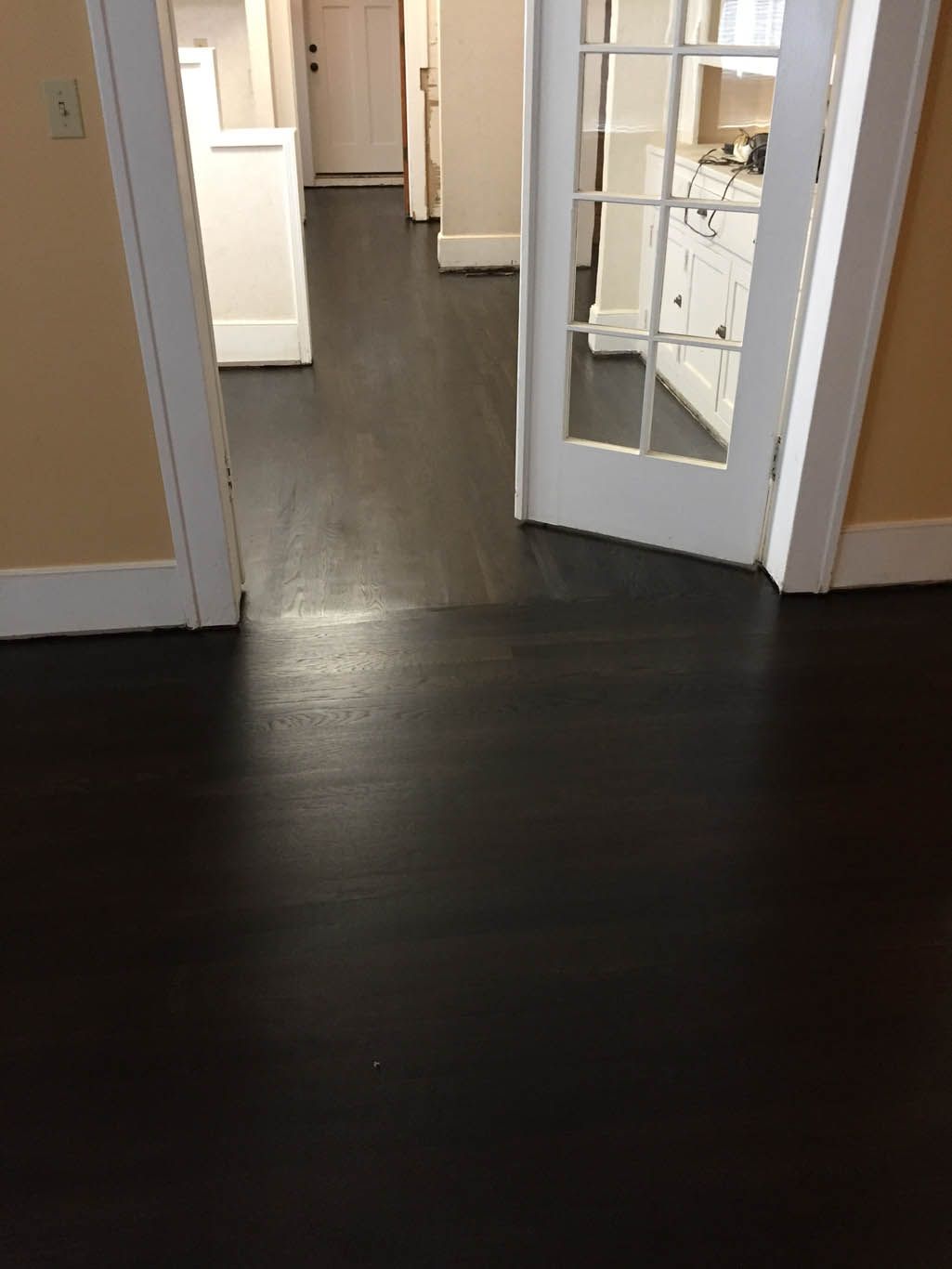A dark wooden floor with a french door leading to a kitchen.
