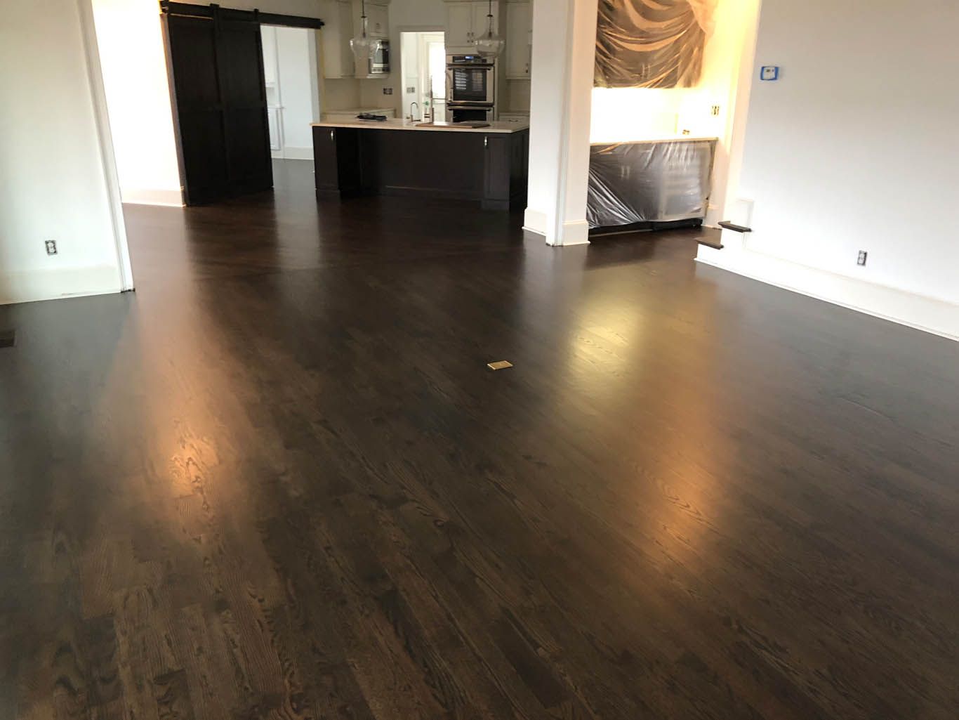 A living room with hardwood floors and a kitchen in the background.