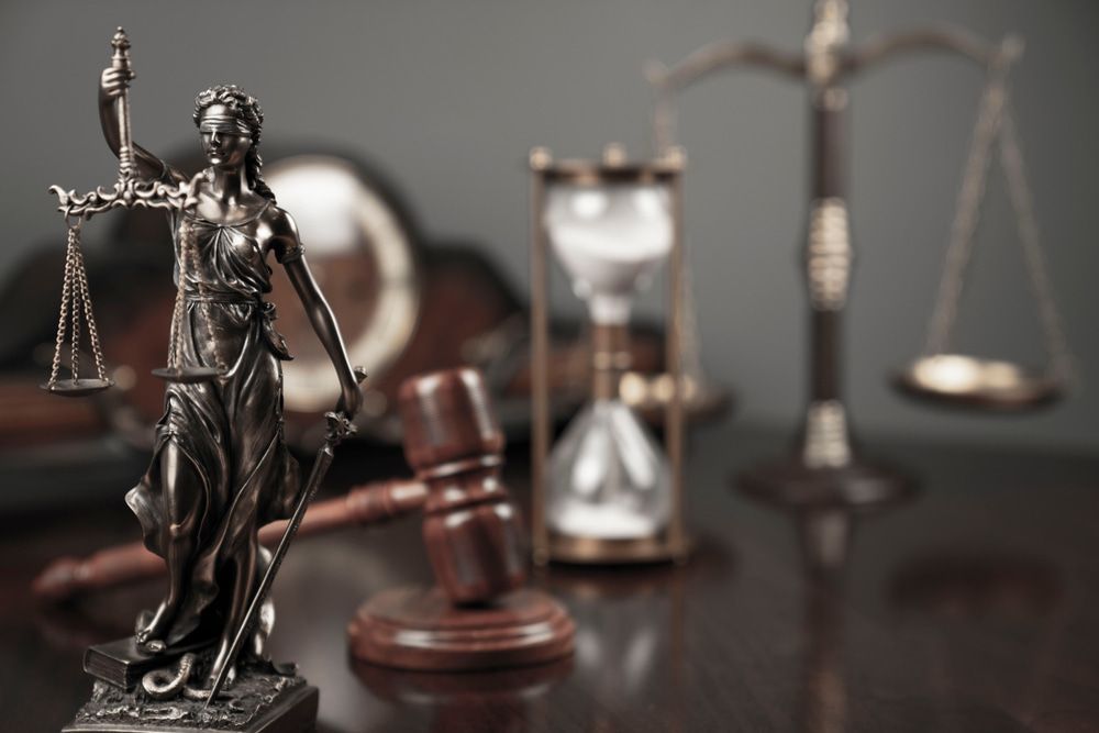 A Statue Of Justice Is Sitting On A Wooden Table Next To A Gavel And Hourglass — McNeilly Lawyers In Kempsey, NSW