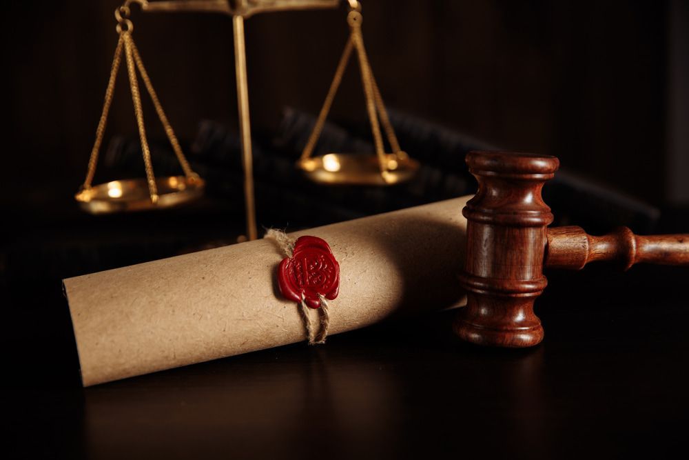 A Wooden Judges Gavel Is Sitting Next To A Sealed Scroll And Scales Of Justice — McNeilly Lawyers In Kempsey, NSW