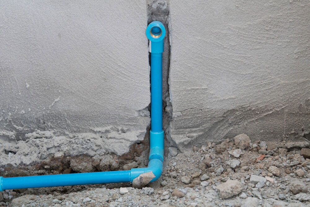 A Blue Pvc Pipe Is Sitting In The Dirt Next To A Wall — Advantage Plumbing Solutions In Newcastle, NSW