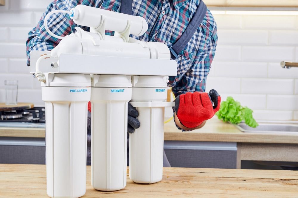 A Man Is Fixing A Water Filter In A Kitchen — Advantage Plumbing Solutions In Belmont, NSW