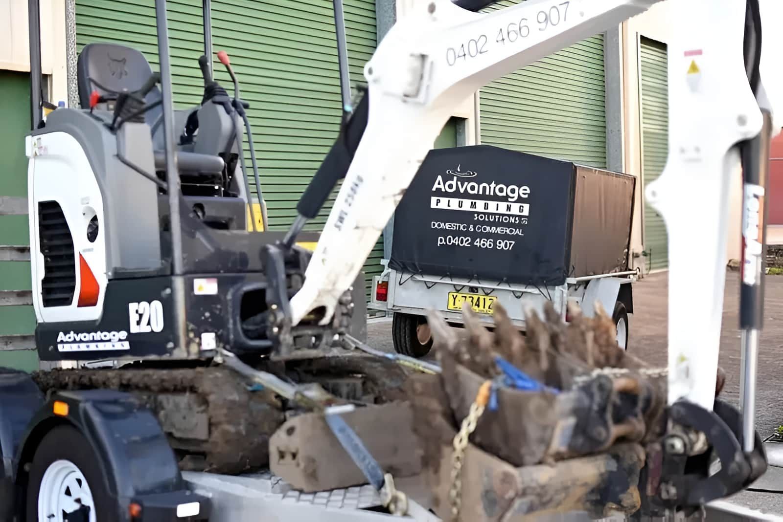 A Small Excavator Is Sitting On Top Of A Trailer — Advantage Plumbing Solutions In Gateshead, NSW
