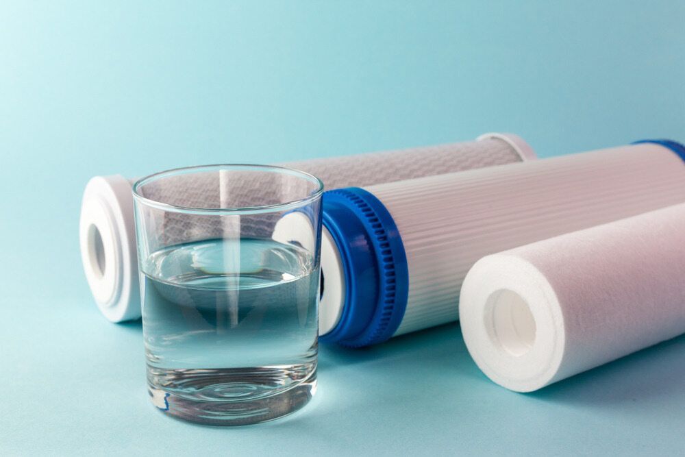 A Glass Of Water Is Sitting Next To Three Water Filters — Advantage Plumbing Solutions In Newcastle, NSW