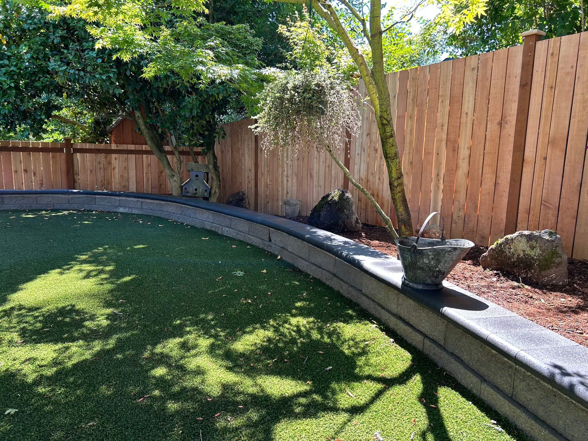 A wooden fence surrounds a lush green lawn in a backyard.