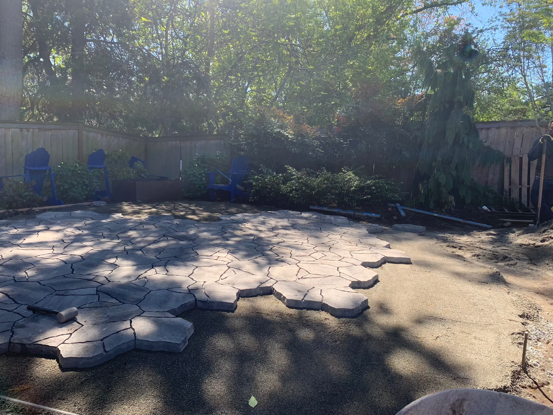 A patio is being built in a backyard with a fence and trees in the background.