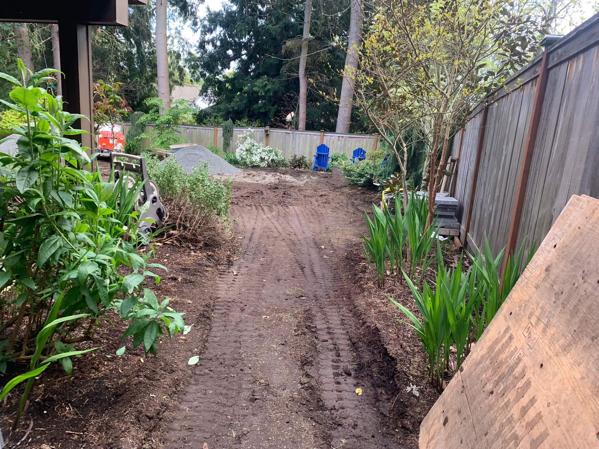 A dirt road going through a garden with a fence in the background.
