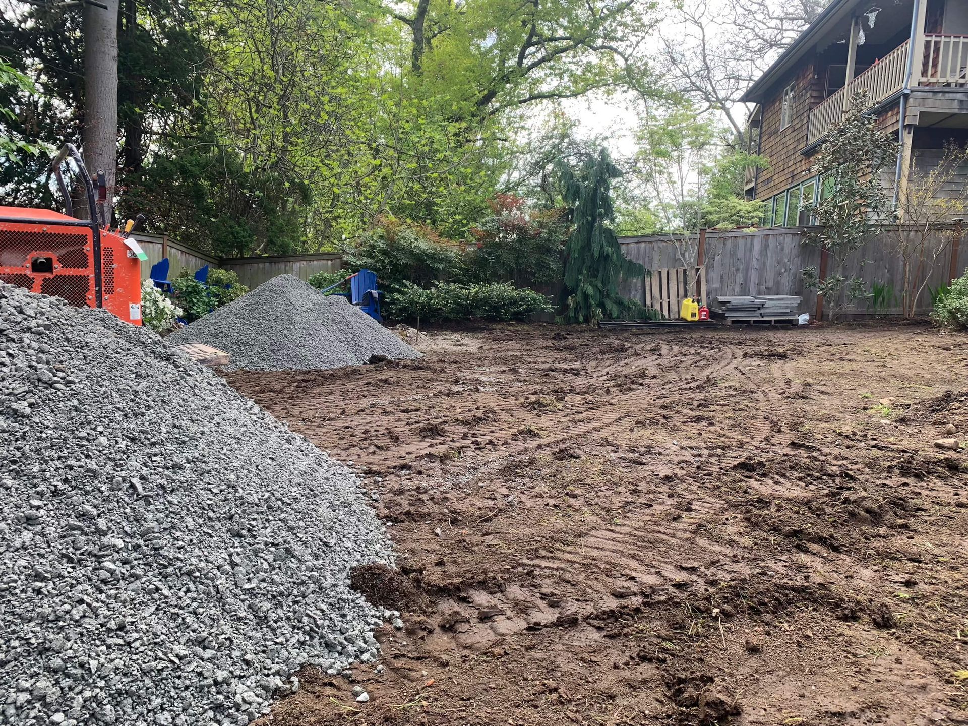 A pile of gravel is sitting in the middle of a dirt field in front of a house.