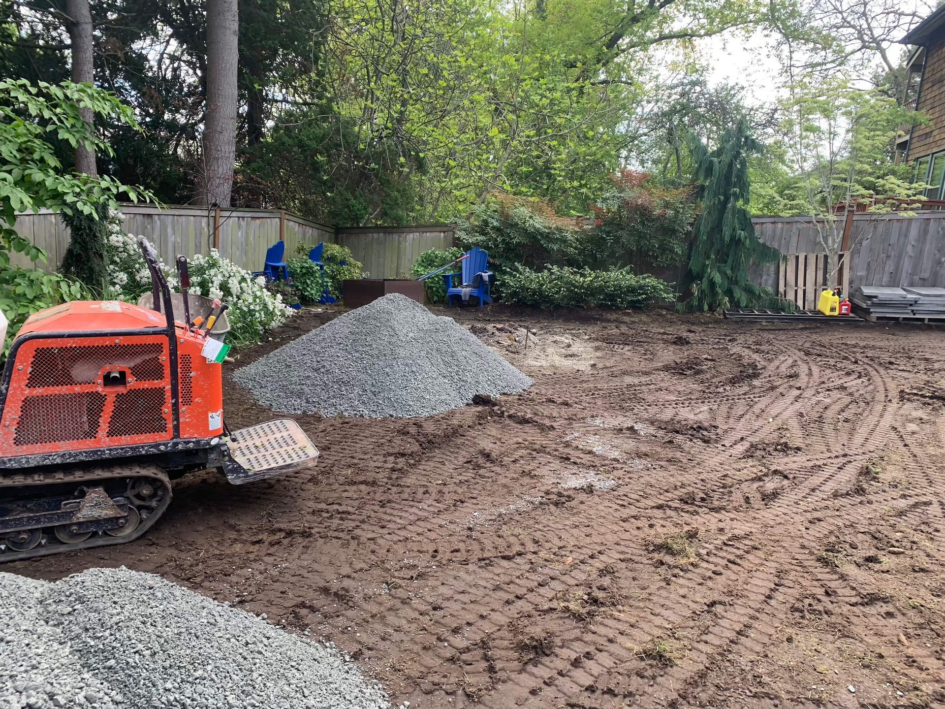 A bulldozer is moving dirt and gravel in a backyard.
