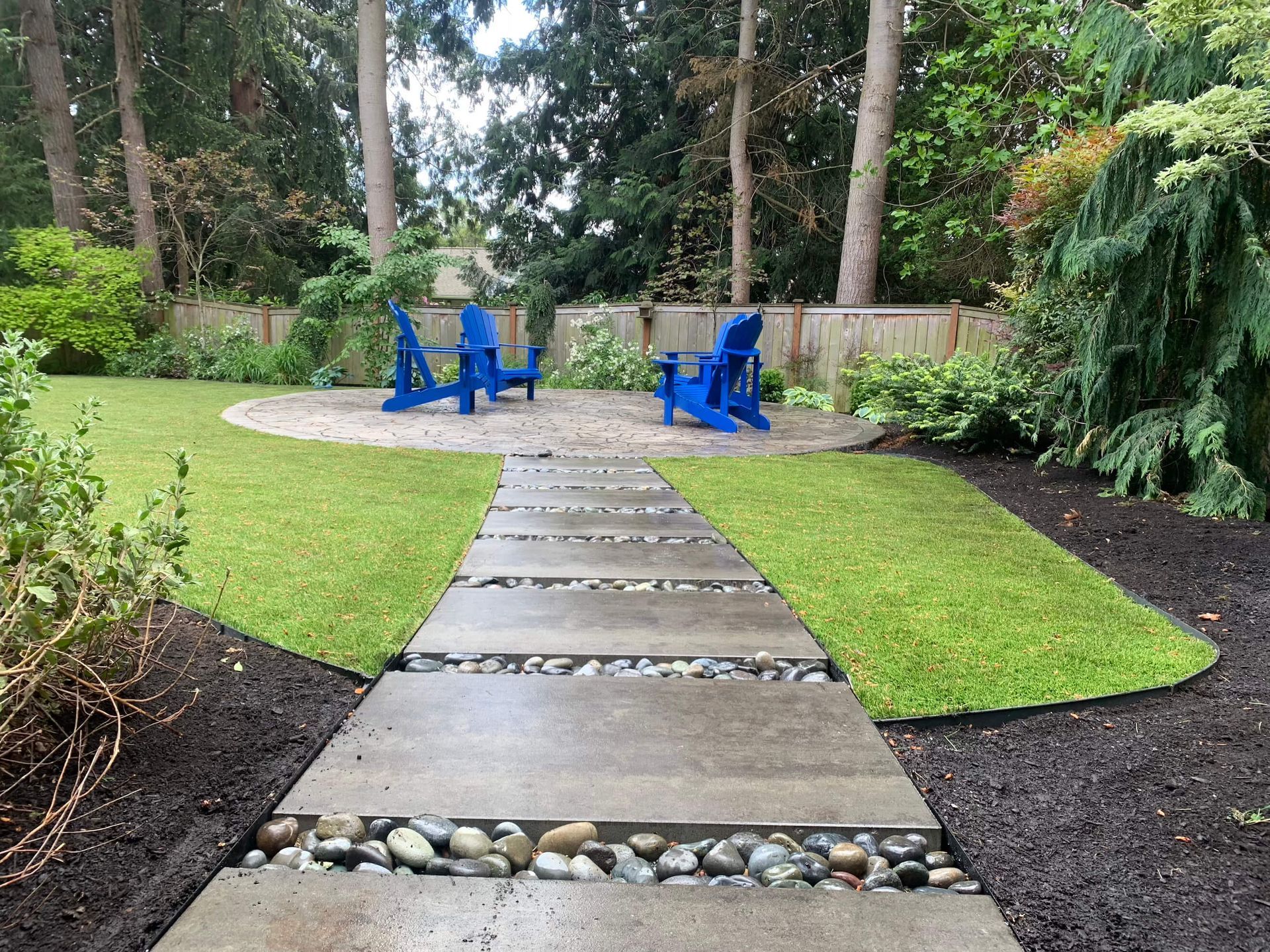A concrete walkway leading to a lawn with blue chairs.
